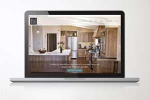 A laptop screen displaying the website of Seelos Design and Construction, showcasing a beautifully remodeled kitchen with wood cabinetry and modern design elements.