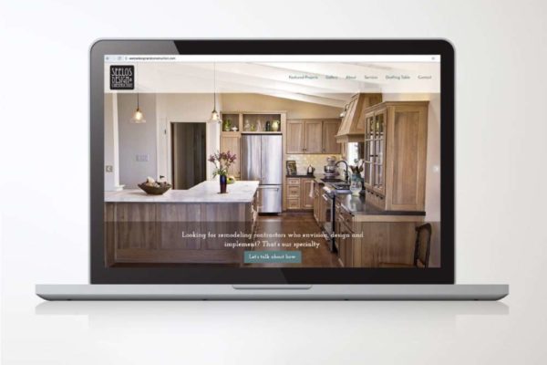 A laptop screen displaying the website of Seelos Design and Construction, showcasing a beautifully remodeled kitchen with wood cabinetry and modern design elements.